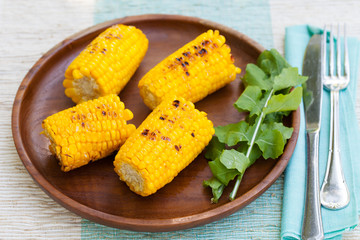 Grilled corn on the cob with salt and butter on a wooden plate