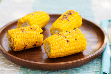 Grilled corn on the cob with salt and butter on a wooden plate