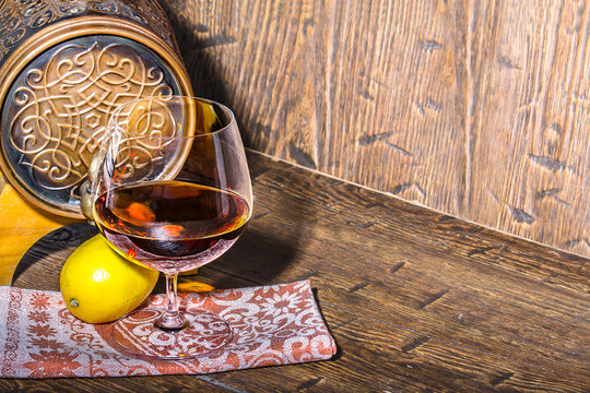 Barrel with lemon and a glass of cognac on the old table