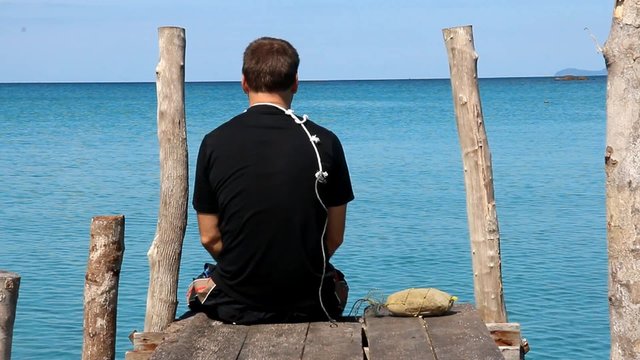 sitting man turning back on a pier over the sea with a noose around his neck