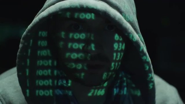  Male hacker working on a computer while green code characters reflect on his face in a dark office room. Shot on RED Cinema Camera.