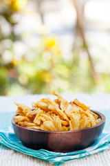 Dried dehydrated deep fried pineapple chips in a wooden bowl on a textile background