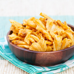 Dried dehydrated deep fried pineapple chips in a wooden bowl on a textile background