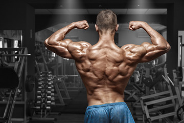 Fototapeta na wymiar Rear view muscular man posing in gym, showing back and biceps. Strong male naked torso, working out