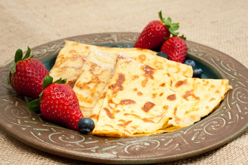 Fresh home made pancakes served on a rustic plate with strawberries and blueberries.