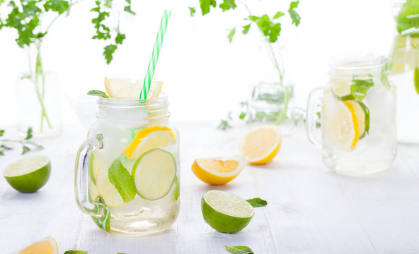 Lemonade with ice, lemon and lime slices in a jar with straw in a white summer wooden background
