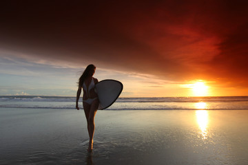 Fototapeta na wymiar Surfer girl on beach at sunset