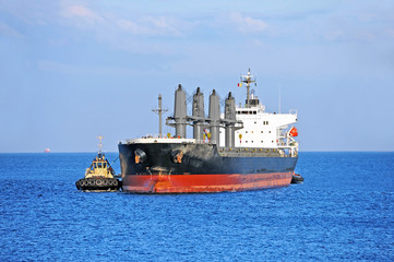 Tugboat assisting bulk cargo ship to harbor quayside