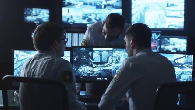 Group of security officers are having a conversation at work in a dark monitoring room filled with display screens. Shot on RED Cinema Camera.