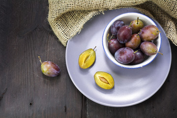 fresh plums in a bowl and on a plate on a dark wooden table