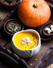 Pumpkin soup with salty popcorn in a white ceramic bowl with fresh pumpkin on a wooden background 