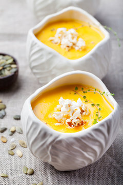Pumpkin,corn soup with salty popcorn in a white ceramic bowl on a wooden background