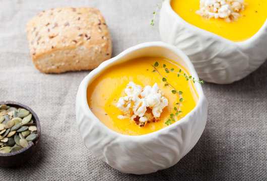 Pumpkin,corn soup with salty popcorn in a white ceramic bowl on a wooden background