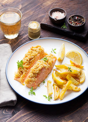 Fish salmon with crumple on top with baked potatoes and lemon slices on a wooden background