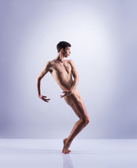 Athletic ballet dancer in a perfect shape performing over the grey background.