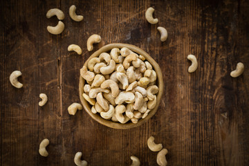 Raw cashew nuts in bowl on textured wooden background, table top view, selective focus