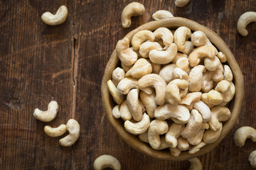 Raw cashew nuts in bowl on textured wooden background, table top view, selective focus