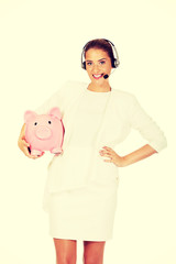 Young businesswoman in headset holding piggybank