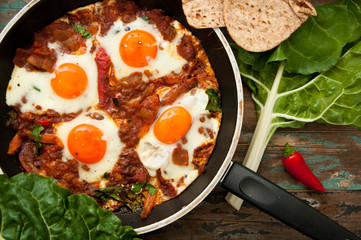 Shakshuka, a dish of eggs poached in a sauce of tomatoes, chili peppers, and onions, spiced with...