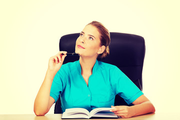 Young female doctor or nurse sitting behind the desk and thinking about something