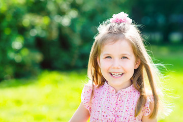 Cute smiling little girl with long blond hair, outdoor portrait on sunny day in summer day