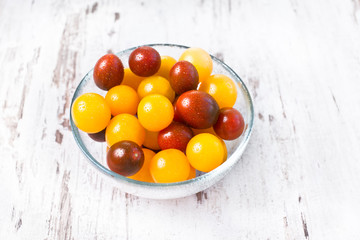 Brown and yellow fresh cherry tomatoes with water drops in glass bowl on wooden table