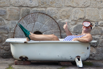 Man with snorkeling gear lying in the bathtub outside