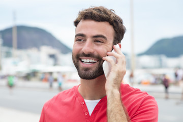 Lachender Mann mit Bart im roten Shirt am Telefon
