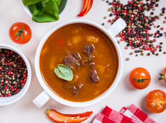 Tomato soup with meat in a white bowl on a white wooden backgrou