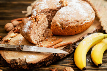 
pastries, cake with walnuts and a banana with powdered sugar on a wooden background