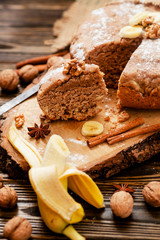 
pastries, cake with walnuts and a banana with powdered sugar on a wooden background
