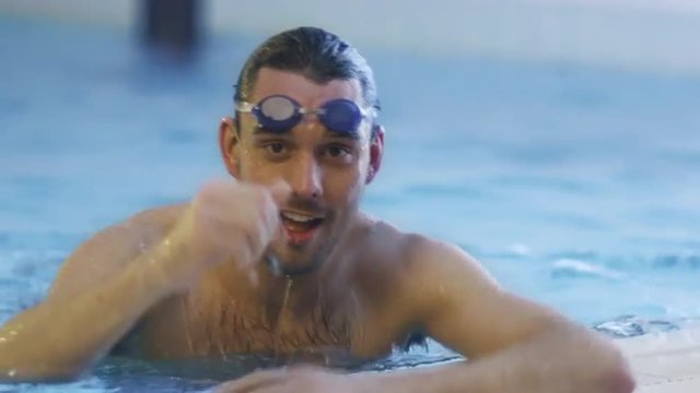 Professional Swimmer in Goggles Getting out the Water in Swimming Pool. Shot on RED Cinema Camera.