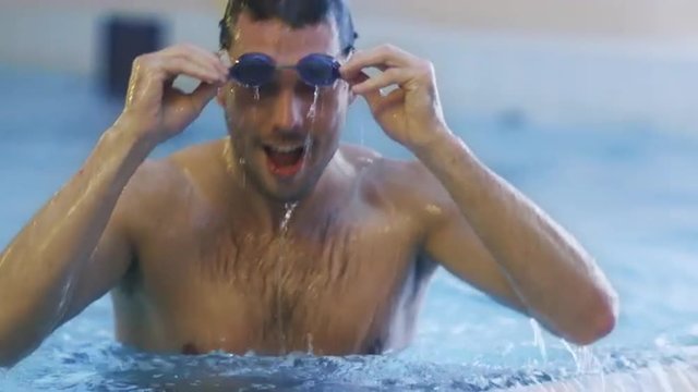 Happy Professional Swimmer in Goggles Getting out the Water in Swimming Pool. Shot on RED Cinema Camera.