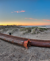 Tight view of dredge pipes lying across the sandy beach. 