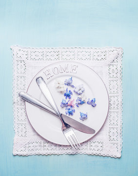 White Table Setting With Home Plate, Cutlery, Lace Doily Napkin  And Petal  Flowers On Blue Shabby Chic Wooden Background, Top View.