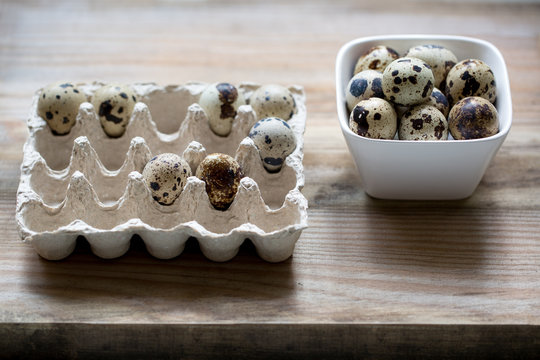 Quail eggs in container and in bowl on rustic wooden background