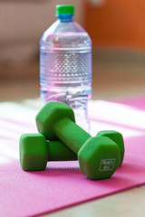Two dumbbells with mineral water on yoga mat