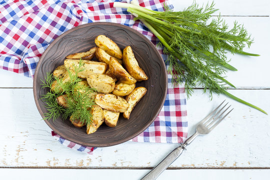 Delicious baked fried potatoes with dill in white plate on table
