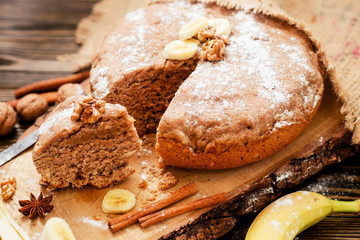 
pastries, cake with walnuts and a banana with powdered sugar on a wooden background