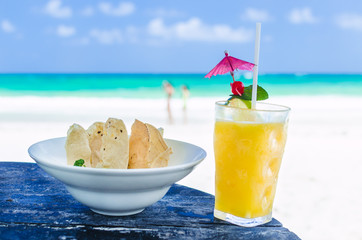 Fresh cold tasty alcohol cocktail with orange juice, tequila, lime, ice and mexican nachos with guacamole sauce close-up with people on background at tropical exotic sandy beach in the Caribbean sea
