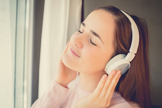 Young womanl enjoying music in headphones at home relaxing. Relaxedstudent girl listening to music with earphones with eyes closed looking serene and happy.