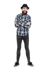 Laughing hipster wearing fedora black hat with crossed arms looking at camera. Full body length portrait isolated over white studio background.