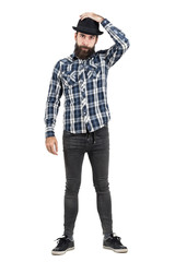 Bearded hipster putting on black fedora hat looking at camera. Full body length portrait isolated...