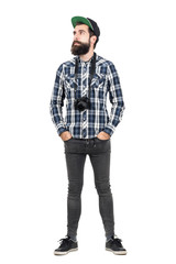 Relaxed hipster wearing black dslr camera over neck with hands in pockets. Full body length portrait isolated over white studio background.