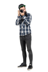 Hipster in plaid shirt taking photo with dslr camera looking at camera. Full body length portrait isolated over white studio background.