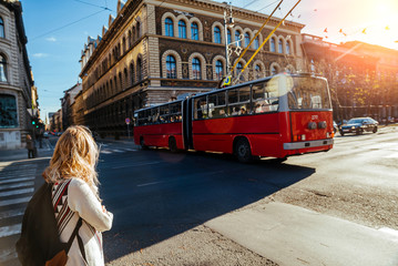 unknown girl with a backpack at the intersection waiting to cross the road and looking at a passing trolleybus, Hungary, Budapest, autumn 2015.