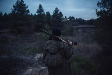brutal hunter, bearded man in warm hat with a gun in his hand, a knife a backpack and smoking pipe...