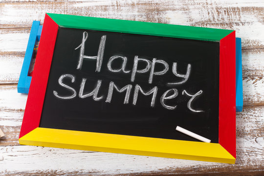Blackboard with text it's Happy summer on wooden deck