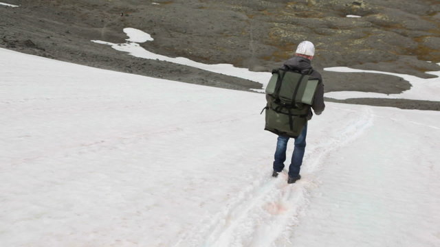 Hiker sliding down the slope on the legs, snow covered mountain pass. Khibiny massife, Kola peninsula, Russia

