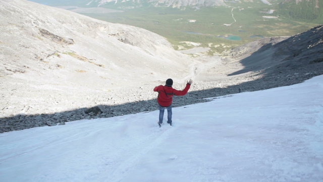 Young hiker sliding the snowy steep slope on the boots, mountains. Khibiny massif, Kola peninsula, Russia
